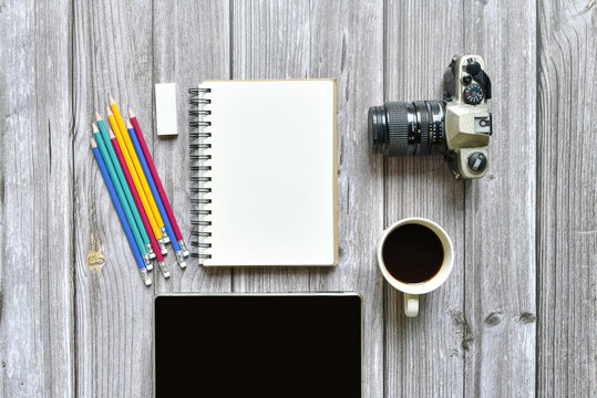 Still life, business or traveler memo concept, Top view image of open notebook with vintage camera coffee colorful pencil and tablet with blank pages on old brown wooden background, for adding text