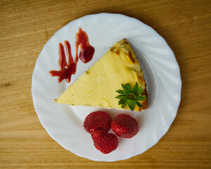 Slice of tasty cheesecake with 3 strawberries and Strawberry sauce drip in a white dish. Top View