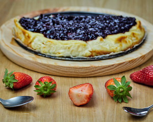 Half of Delicious Cheesecake on a round wooden plate and several strawberries and two spoons.