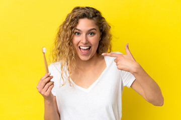 Young caucasian woman holding a brushing teeth isolated on yellow background giving a thumbs up gesture