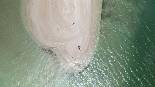 Ascending aerial view of a young woman laying on the white sand beach of No Man Land, Tobago