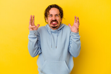 Young caucasian man isolated on yellow background screaming with rage.
