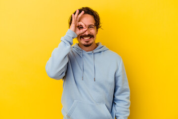 Young caucasian man isolated on yellow background excited keeping ok gesture on eye.