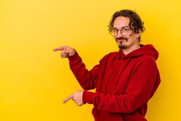 Young caucasian man isolated on yellow background pointing with forefingers to a copy space, expressing excitement and desire.