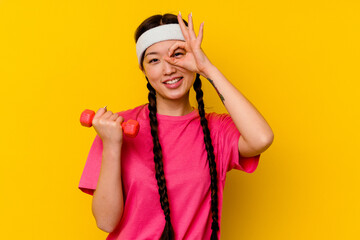 Young sport chinese woman isolated on yellow background excited keeping ok gesture on eye.