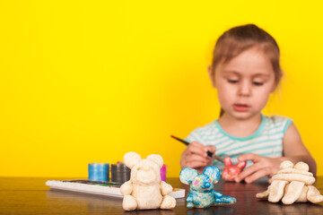 Little girl paints toy animals paints on a yellow background