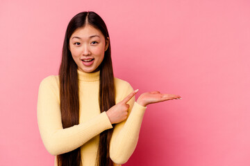 Young chinese woman isolated on pink background excited holding a copy space on palm.