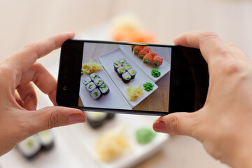 Woman taking photo of tasty sushi set
