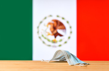 A medical mask lies on the table against the background of the flag of Mexico. The concept of a mandatory mask regime for residents of the country and tourists in Mexico during a pandemic.