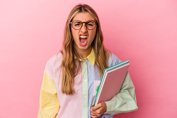 Young caucasian blonde student woman holding books isolated screaming very angry and aggressive.
