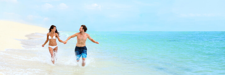 Beach couple Caribbean vacation summer travel fun splashing water running in fit bikini body. Happy...
