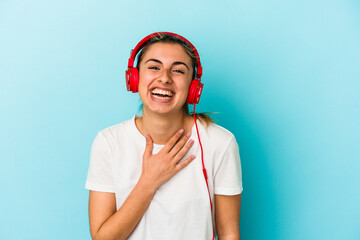 Young blonde woman listening to music on headphones isolated on blue background laughs out loudly keeping hand on chest.