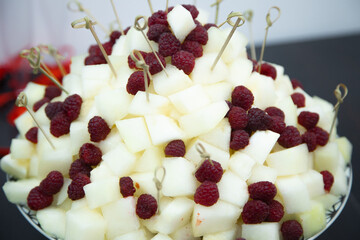 Fruit plate consisting of chopped melon and decorated with raspberries.