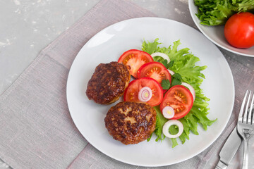Fried meat cutlets with tomatoes and salad on a plate.