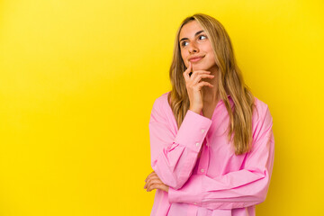 Young blonde caucasian woman isolated on yellow background relaxed thinking about something looking at a copy space.
