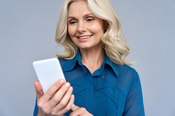 Happy smiling mature 50 years age blonde woman manager looking at cellphone using online mobile...