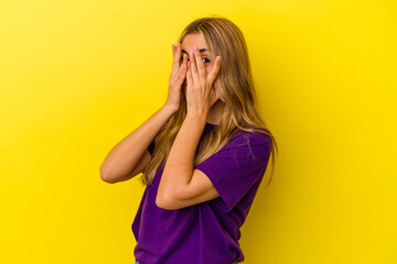 Young blonde caucasian woman isolated on yellow background blink through fingers frightened and nervous.