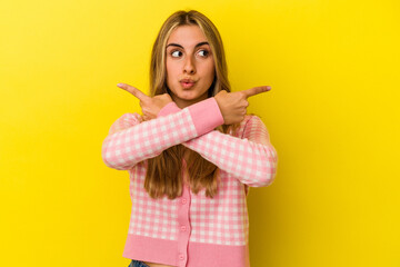 Young blonde caucasian woman isolated on yellow background points sideways, is trying to choose between two options.