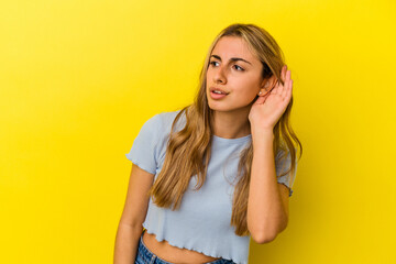 Young blonde caucasian woman isolated on yellow background trying to listening a gossip.