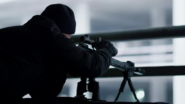 Killer adjusting sight on sniping rifle. Sniper preparing weapon for shooting