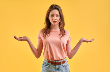 A beautiful girl in casual clothes holds two hands, on the palms there is an empty space for a product, choice, compare, isolated on a yellow background.