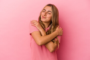 Young blonde caucasian woman isolated on pink background hugs, smiling carefree and happy.