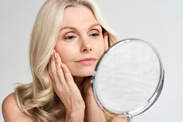 Closeup portrait of gorgeous happy middle age woman looking at mirror touching her skin enjoying...