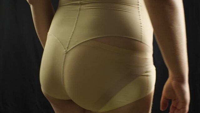 A chubby girl in shapewear is spinning around her axis. The underwear provides maximum slimming effect in the abdominal area. Black background