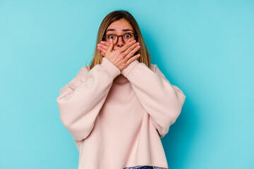 Young student caucasian woman isolated on blue background shocked covering mouth with hands.