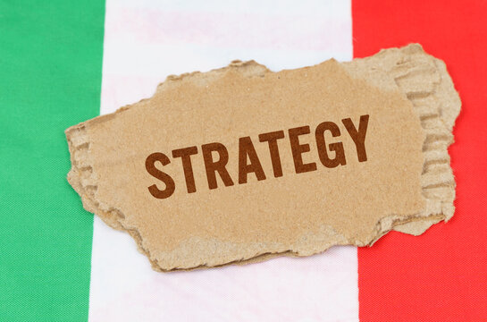 Against the background of the flag of Italy lies cardboard with the inscription - Strategy - Powered by Adobe