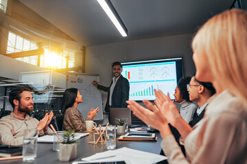 A group of successful business people applaud the speaker at the presentation. Project, finance, teamwork. In the center, a man writes on a flipchart and talks to colleagues.