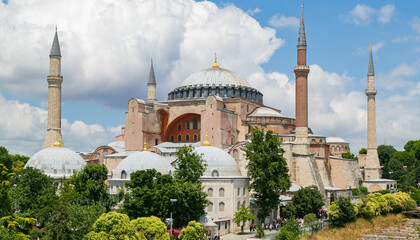 Fototapeta na wymiar Hagia Sophia in summer, Istanbul, Turkey. The world famous monument of Byzantine architecture, imperial mosque and now a museum. View of the St. Sophia Cathedral with cloudy sky and green trees.