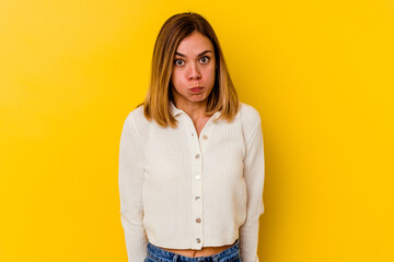 Young caucasian skinny woman isolated on yellow background shrugs shoulders and open eyes confused.