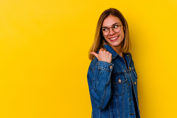 Young caucasian skinny woman isolated on yellow background points with thumb finger away, laughing and carefree.