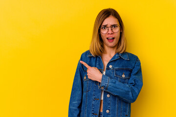 Young caucasian skinny woman isolated on yellow background smiling and pointing aside, showing something at blank space.