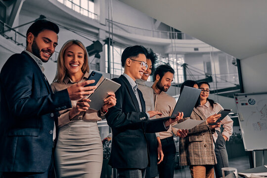 A Group Of Business People Use Digital Tablets, Laptops, Phones And Documents While Standing In The Office. The Concept Of Work, Business, Meeting.