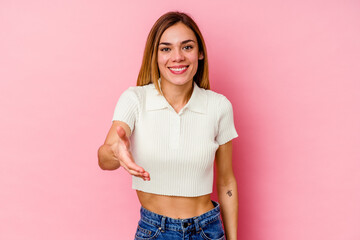 Young caucasian woman isolated on pink background stretching hand at camera in greeting gesture.