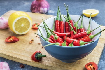 red chili pods in bowl with lemon and garlic on wooden chopping board, close-up