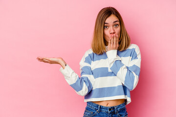 Young caucasian woman isolated on pink background impressed holding copy space on palm.