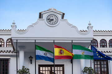 The flag of Spain, the flag of Andalusia, the flag of the European Union against the background of the faiths with a clock. Andalusia Mijas Pueblo - obrazy, fototapety, plakaty