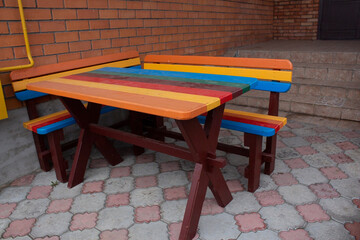 Colorful wooden table and picnic bench near the house on the background of a brick wall.