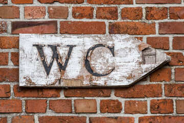 altes WC Schild aus Holz  an einer Backsteinwand, das nach rechts zeigt