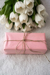 white tulips and pink gift in craft rope on white background