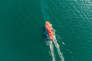 The pilot boat orange goes to meet the vessel on the outer roads. Helicopter view. Top view of the sea.