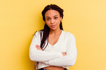 Young african american woman isolated on yellow background frowning face in displeasure, keeps arms...
