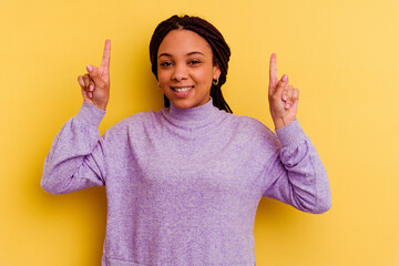 Young african american woman isolated on yellow background indicates with both fore fingers up...