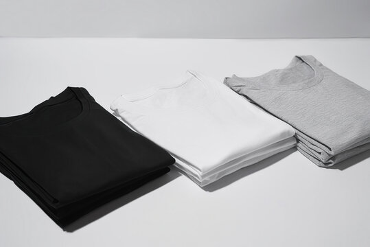 Three folded monochrome t shirts gray, black and white isolated over gray background