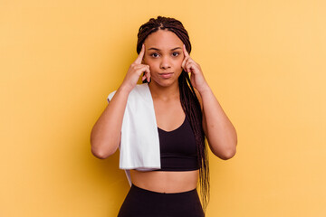 Young sport african american woman holding a towel isolated on yellow background focused on a task, keeping forefingers pointing head.