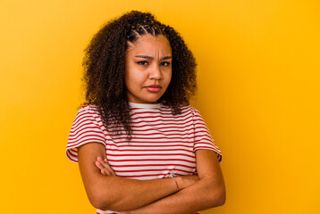 Young african american woman isolated on yellow background frowning face in displeasure, keeps arms...