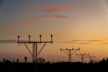 Silhouette of runway signs during sunset. In the sky we can see red clouds as if they were fire. We can also see the control tower in the background.